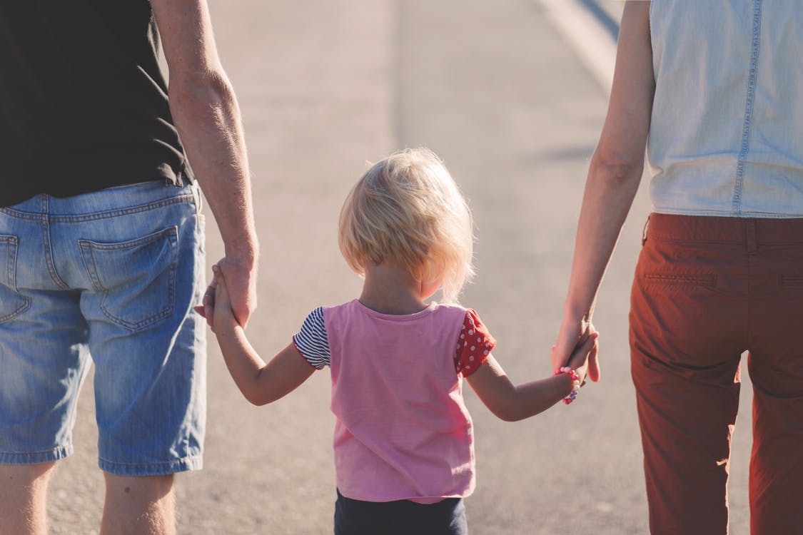 Image with a father and a mother holding the hands of their little daughter